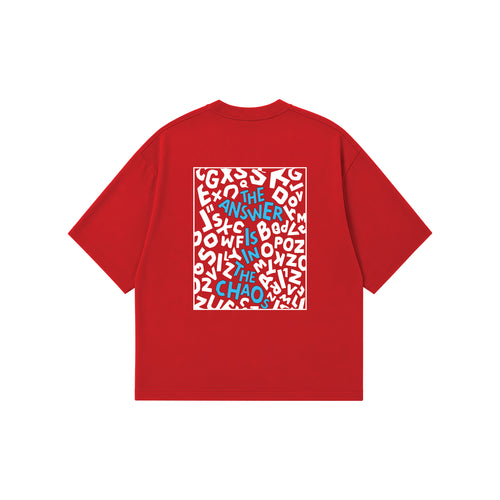 A red short-sleeve t-shirt with a square graphic print on the back, featuring a white background filled with white abstract shapes and blue text that reads 'THE ANSWER IS IN THE CHAOS'.